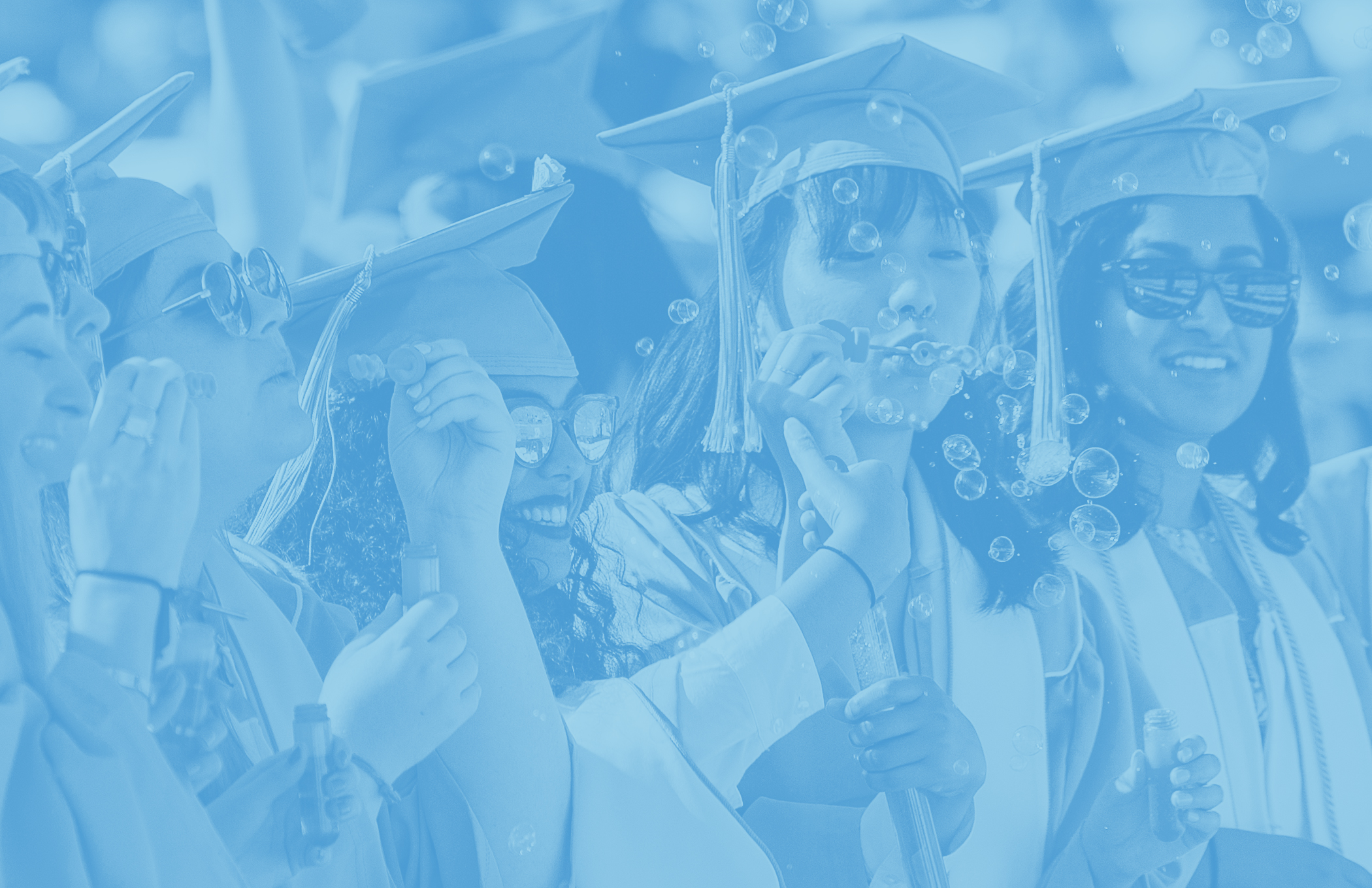 Photo of female graduates at commencement blowing bubbles with Carolina Blue overlay on top of the photo.
