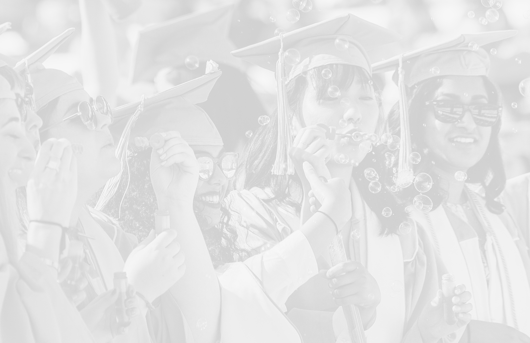 Photo of female graduates at commencement blowing bubbles with light gray overlay on top of the photo.
